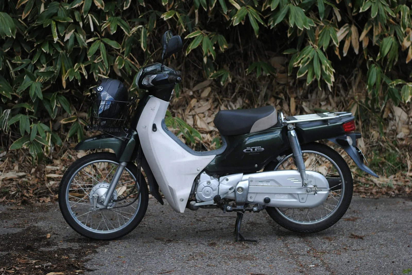 A green-and-white Honda Cub in profile, showing the wheels and step-through frame